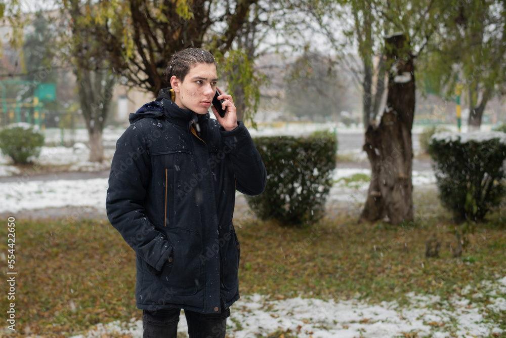 A teenage boy with a serious little angry face is talking on the phone on the street in winter, the boy is depressed and needs to talk A teenage boy with a serious little angry face is talking on the phone on the street in winter, the boy is depressed and needs to talk
