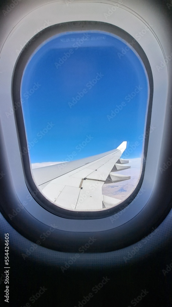 View from the window of the airplane. Rear of the wing. Blue sky. White clouds in the background out of focus. Selective focus. Copy space