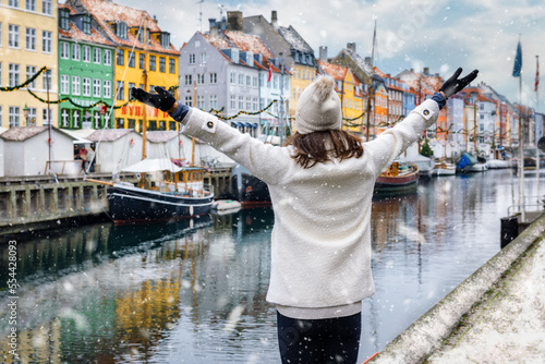 A happy tourist woman enjoys the view to the beautiful Nyhavn area in Copenhagen, Denmark, during winter time with snow and Christmas decorations
