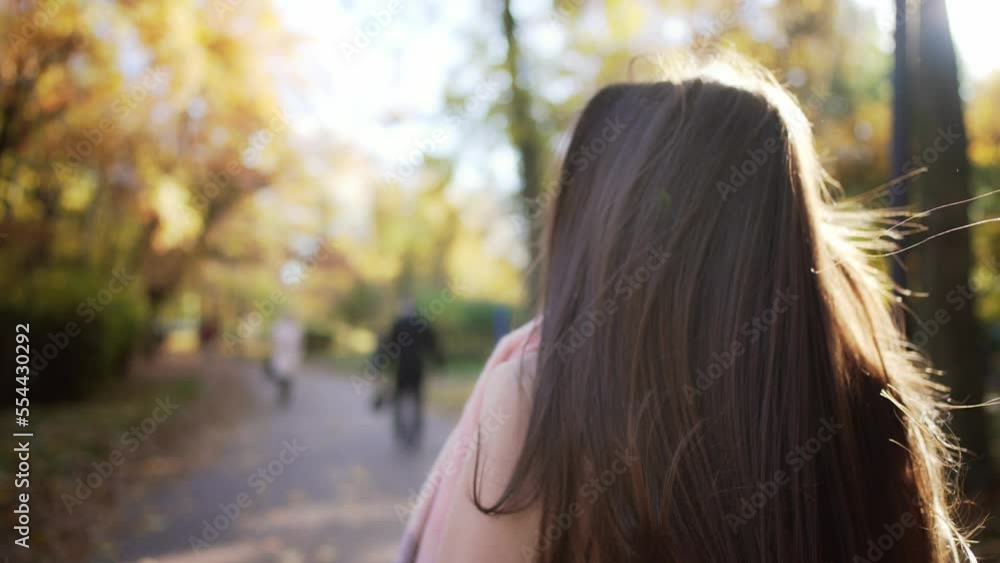 Rear view of girl with glass of coffee in hands go forward in park and waves her long beautiful dark hair to sides. Brunette joyfully skips and enjoy walk in autumn park with glass of coffee in hands. Rear view of girl with glass of coffee in hands go forward in park and waves her long beautiful dark hair to sides. Brunette joyfully skips and enjoy walk in autumn park with glass of coffee in hands.