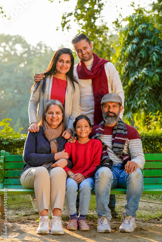 happy Indian family sitting at park in winter wear or warm clothes