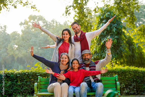 happy Indian family sitting at park in winter wear or warm clothes