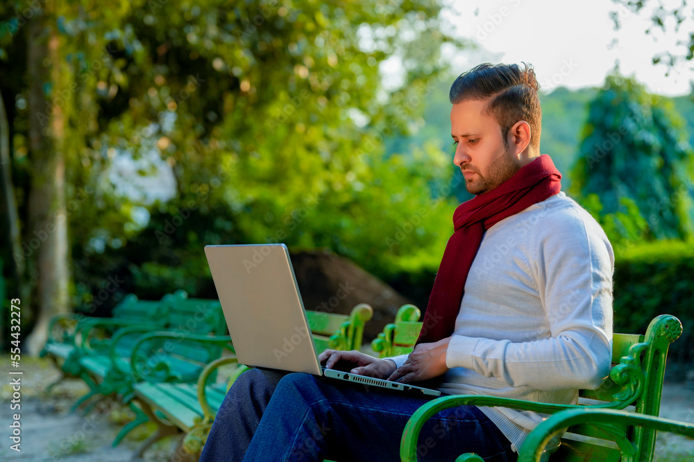 Young indian man in warm wear and working on laptop at park Young indian man in warm wear and working on laptop at park