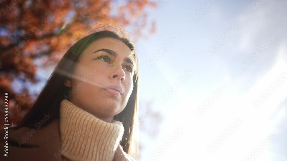 Bottom view close-up portrait of young caucasian girl against blue sky. Woman stands and looks thoughtfully into distance in autumn park or forest with trees and gold yellow foliage. Walk in nature. Bottom view close-up portrait of young caucasian girl against blue sky. Woman stands and looks thoughtfully into distance in autumn park or forest with trees and gold yellow foliage. Walk in nature.