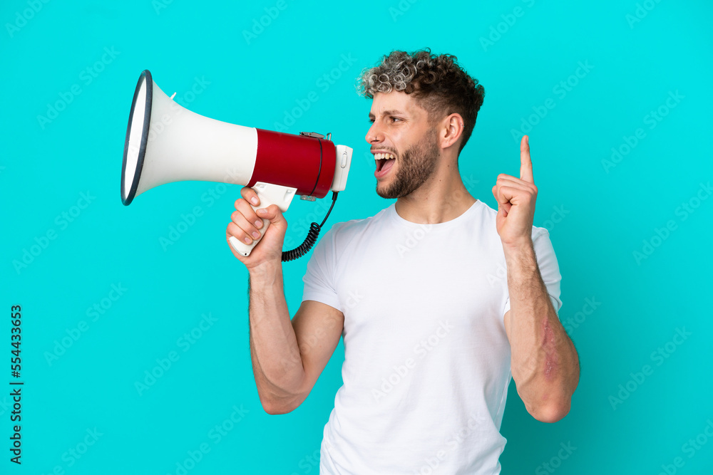 Young handsome caucasian man isolated on blue background shouting through a megaphone to announce something in lateral position Young handsome caucasian man isolated on blue background shouting through a megaphone to announce something in lateral position