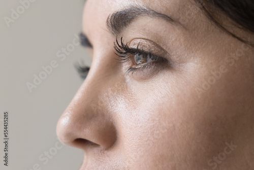 Fototapeta Naklejka Na Ścianę i Meble -  Brown eyes close up of young beautiful black haired woman with healthy smooth skin looking away. Side view, cropped shot. Female model promoting beauty care, cosmetology.