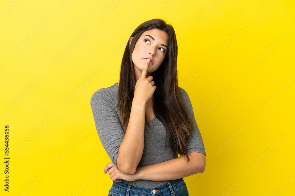 Young Brazilian woman isolated on yellow background having doubts while looking up Young Brazilian woman isolated on yellow background having doubts while looking up