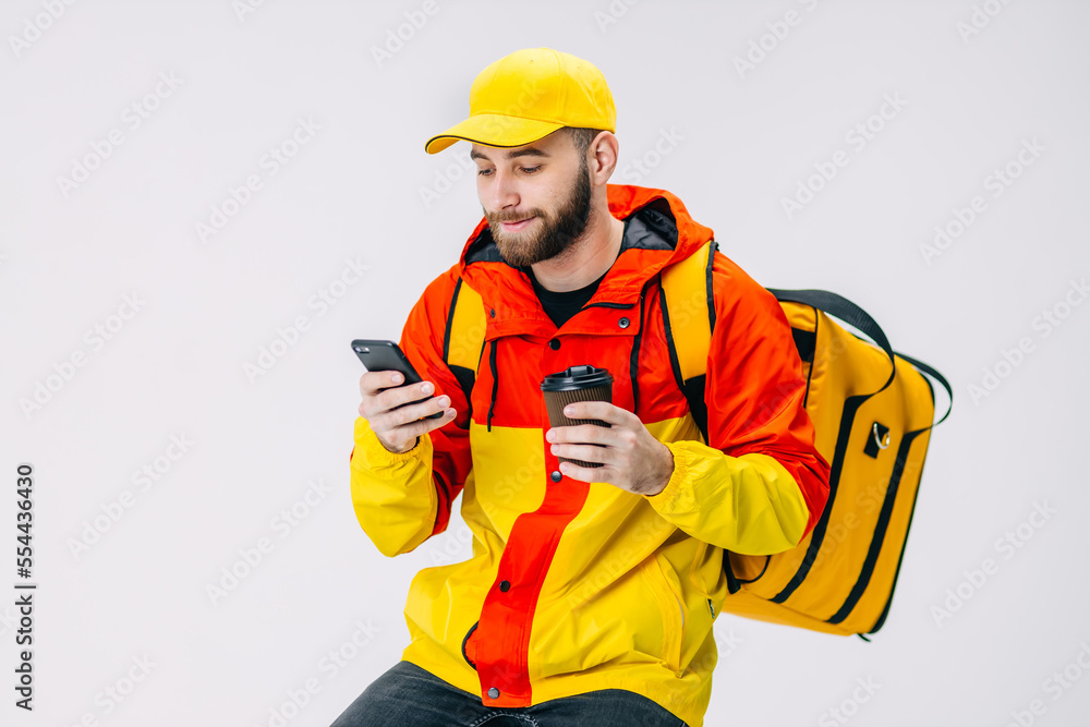 Young courier is drinking coffee while waiting for the order, watching funny videos on the phone.