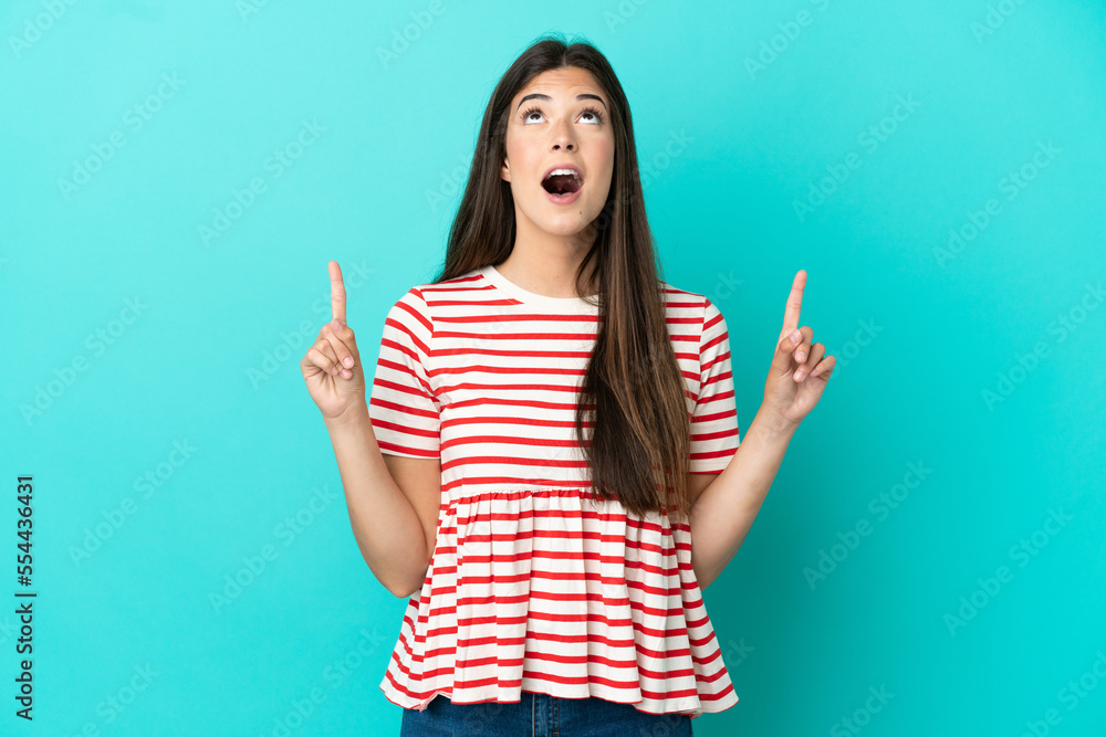 Young Brazilian woman isolated on blue background surprised and pointing up Young Brazilian woman isolated on blue background surprised and pointing up