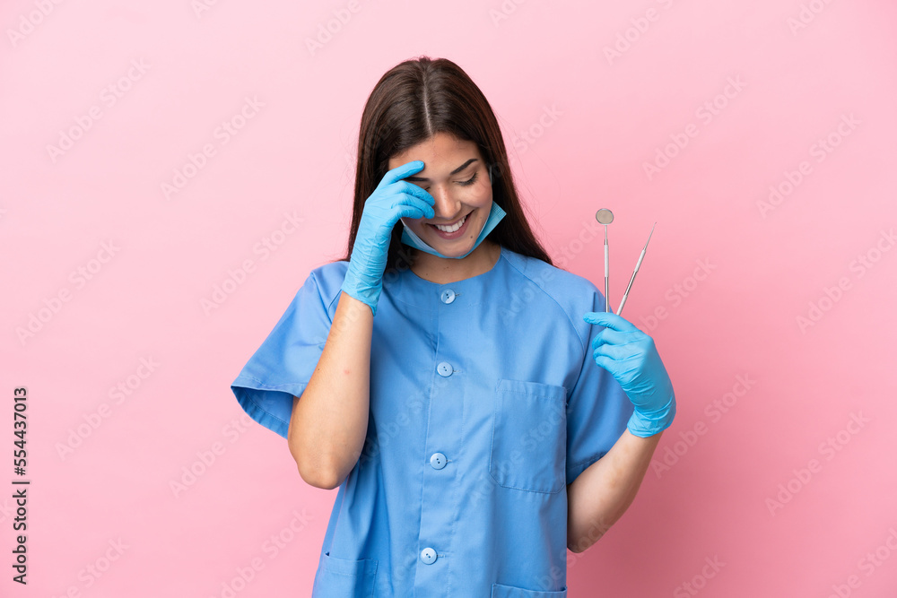 Dentist woman holding tools isolated on pink background laughing Dentist woman holding tools isolated on pink background laughing
