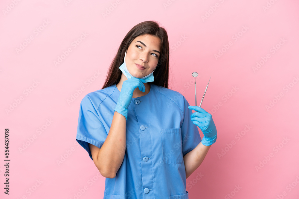 Dentist woman holding tools isolated on pink background and looking up Dentist woman holding tools isolated on pink background and looking up