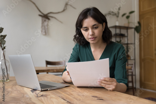 Fototapeta Serious freelance business woman working on report at home, reading document at