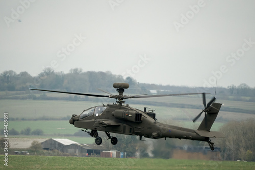 close up rear side view of British army AH-64E Boeing Apache Attack helicopter (ZM722 ArmyAir606) hovering, autumn sky, Wiltshire UK