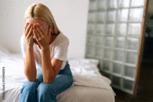 Closeup face of unhappy young woman hiding face in hands, feeling desperate cheated hopeless sitting alone at home. Upset millennial female crying, suffering from consequences of wrong decision.