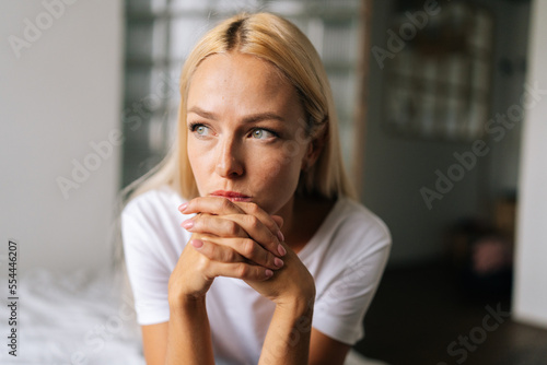 Closeup face of thoughtful woman sitting alone at home and looking away with sad expression holding hands on chin  thinking over problems. Frustrated female pondering make difficult choice.
