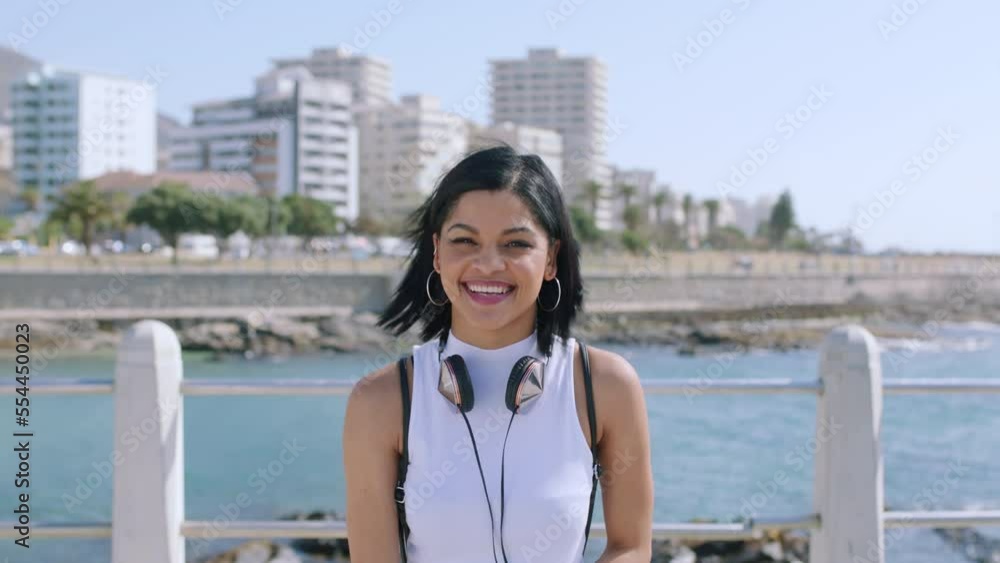 Beach, headphones and face of woman with music for travel, outdoor mental health or youth wellness on holiday vacation. Cityscape, ocean water and a happy Mexico student with audio technology at sea