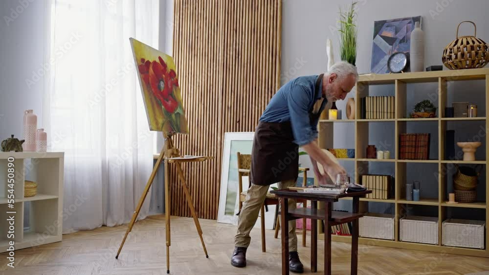 Full-length of elderly painter artist, a young at heart man, paints on canvas in creative art studio Full-length of elderly painter artist, a young at heart man, paints on canvas in creative art studio