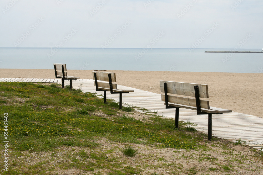 Three benches overlooking a sandy beach and the water on a gloomy, cloudy, overcast day. Image has copy space. Three benches overlooking a sandy beach and the water on a gloomy, cloudy, overcast day. Image has copy space.
