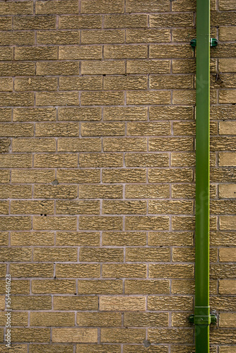 A bright green drainpipe set against the right-hand side of a brown brick wall. Image has copy space on top, bottom, and left-hand side. photo