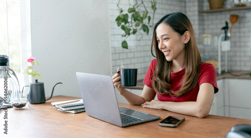 Beautiful young woman working on laptop computer while sitting at the kitchen room, drinking coffee Beautiful young woman working on laptop computer while sitting at the kitchen room, drinking coffee