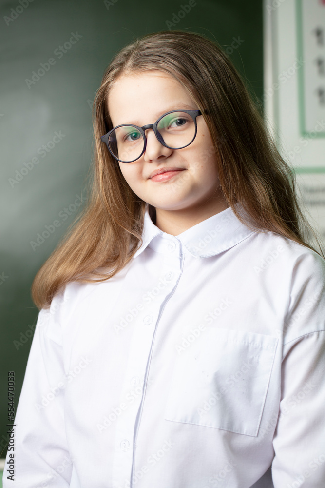 Beautiful girl in glasses of middle school age on the background of the blackboard.