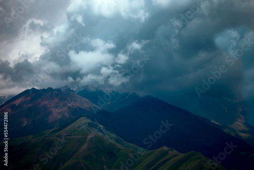 Dark atmospheric surreal landscape with a dark rocky mountain peak in low clouds in a gray cloudy sky. A gray low cloud on a high peak. High black rock in low clouds. Surreal gloomy mountains.