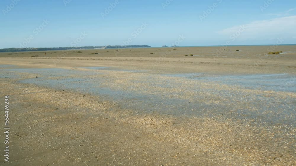 A walk on the vast flat coastline of Saint Benoit Des Ondes, Brittany, France, during low tide. Small shells on the ground with sand. The atlantic ocean is visible in the distance. A walk on the vast flat coastline of Saint Benoit Des Ondes, Brittany, France, during low tide. Small shells on the ground with sand. The atlantic ocean is visible in the distance.