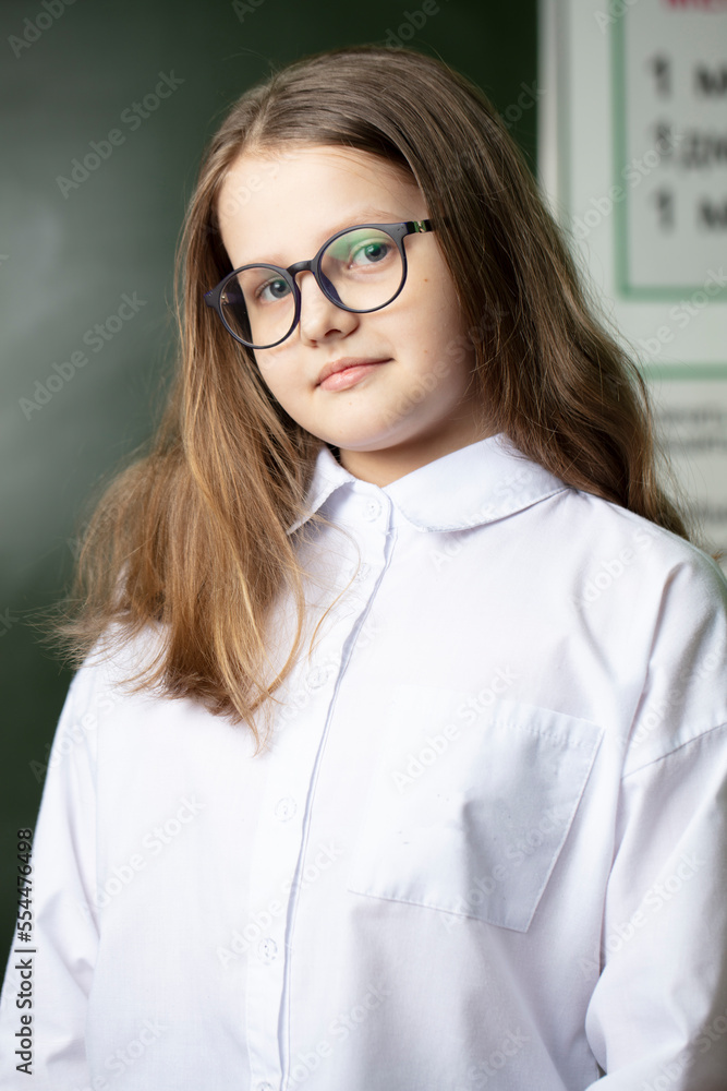 Beautiful girl in glasses of middle school age on the background of the blackboard.
