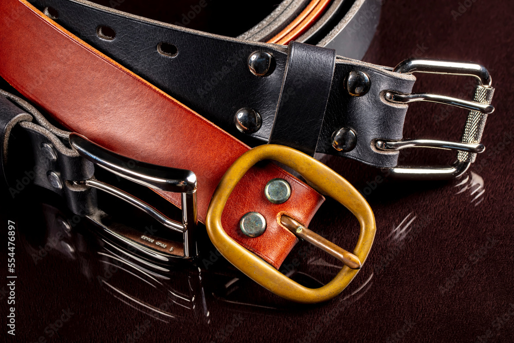 Several leather belts with a metal buckle on a dark background.