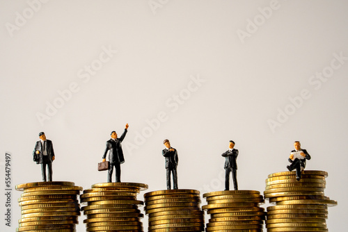 Business Money and Financial Concept. five businessman miniature people figure standing on top of stack of gold coins on white background with copy sapce.