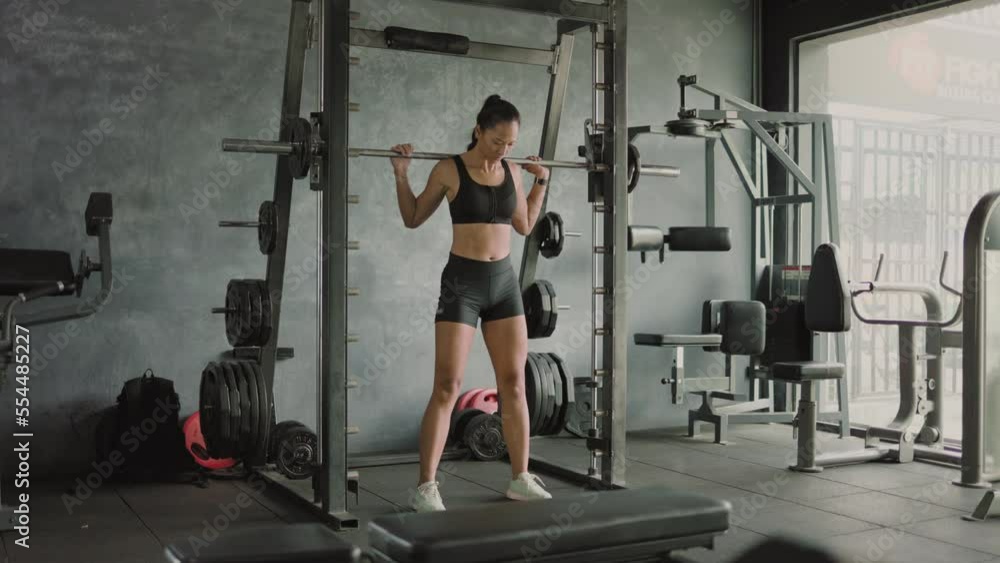 Asian female athlete doing squats in gym with barbell Asian female athlete doing squats in gym with barbell