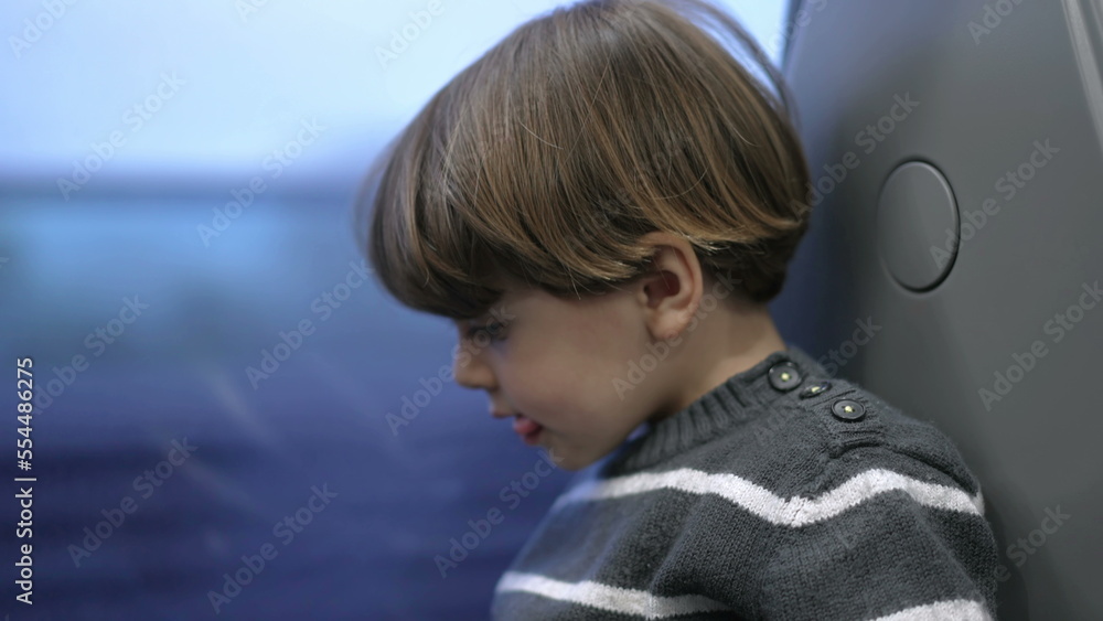 Fototapeta premium One small boy traveling by train staring at window with landscape passing by. Child travels on high speed train