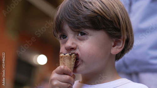 Small boy enjoying ice cream dessert outside in street. Portrait face of kid eating cone