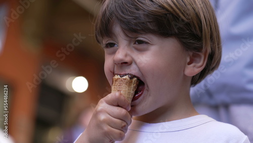 Small boy enjoying ice cream dessert outside in street. Portrait face of kid eating cone