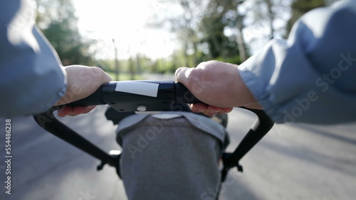 Hands holding stroller POV of mother walking outside in nature with baby. Parent pushing toddler carriage at park