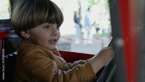 One happy small boy driving toy car interior at amusement park carousel. Child holding steering wheel pretending to drive