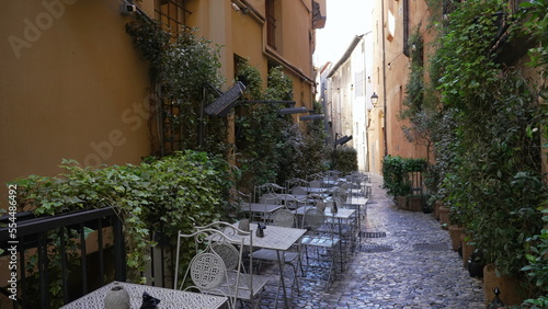 Old European street with tables and chairs on cobblestone urban Italian alley with nobody