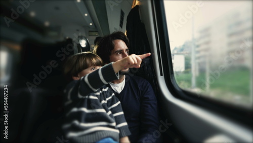 Child seated on father lap pointing finger at landscape while traveling by train. Parent and child staring at window