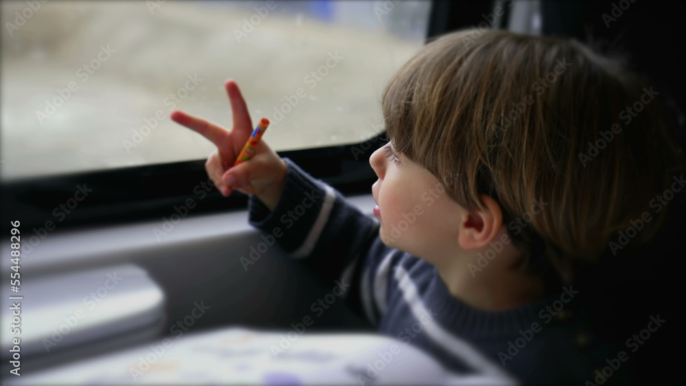 Small passenger child sitting by train window looking at landscape passing by. Excited child in a moving transportation