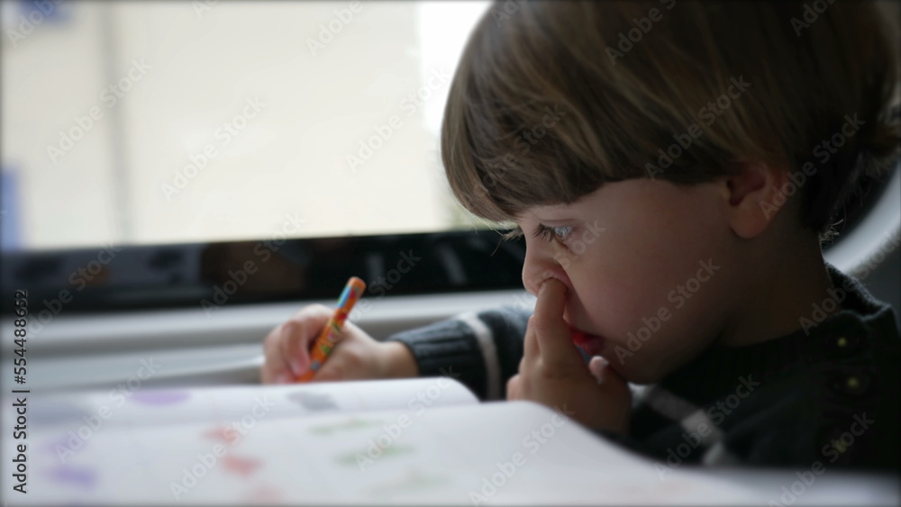 Concentrated Child nose picking while doing homework seated inside on a moving train Concentrated Child nose picking while doing homework seated inside on a moving train