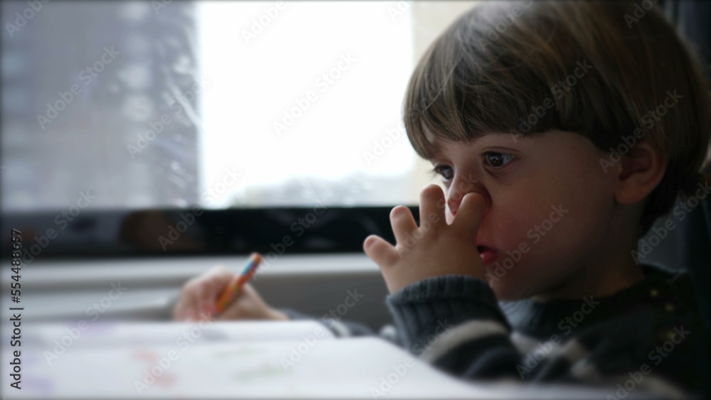 Concentrated Child nose picking while doing homework seated inside on a moving train Concentrated Child nose picking while doing homework seated inside on a moving train