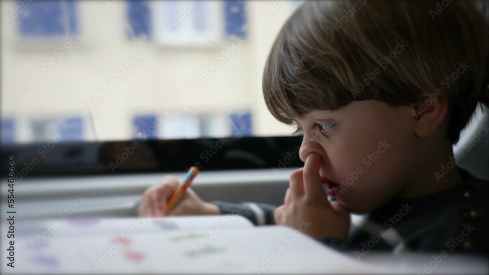 Concentrated Child nose picking while doing homework seated inside on a moving train Concentrated Child nose picking while doing homework seated inside on a moving train