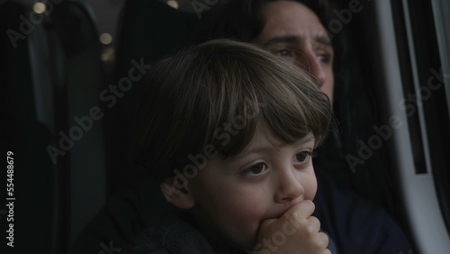 Child seated on father lap traveling by train. Closeup faces of kid and child together
