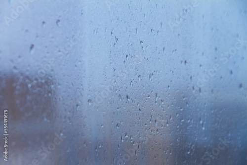 raindrops on blue glass window on cloudy day