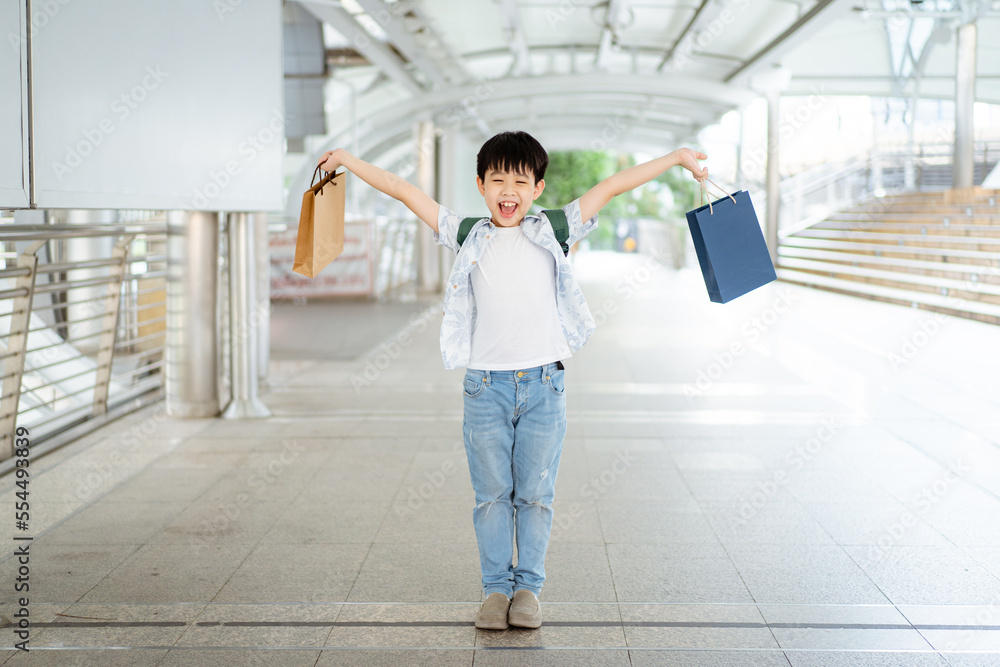 Cheerful happy Asian little boy carrying a paper shopping bags and smiling to camera.