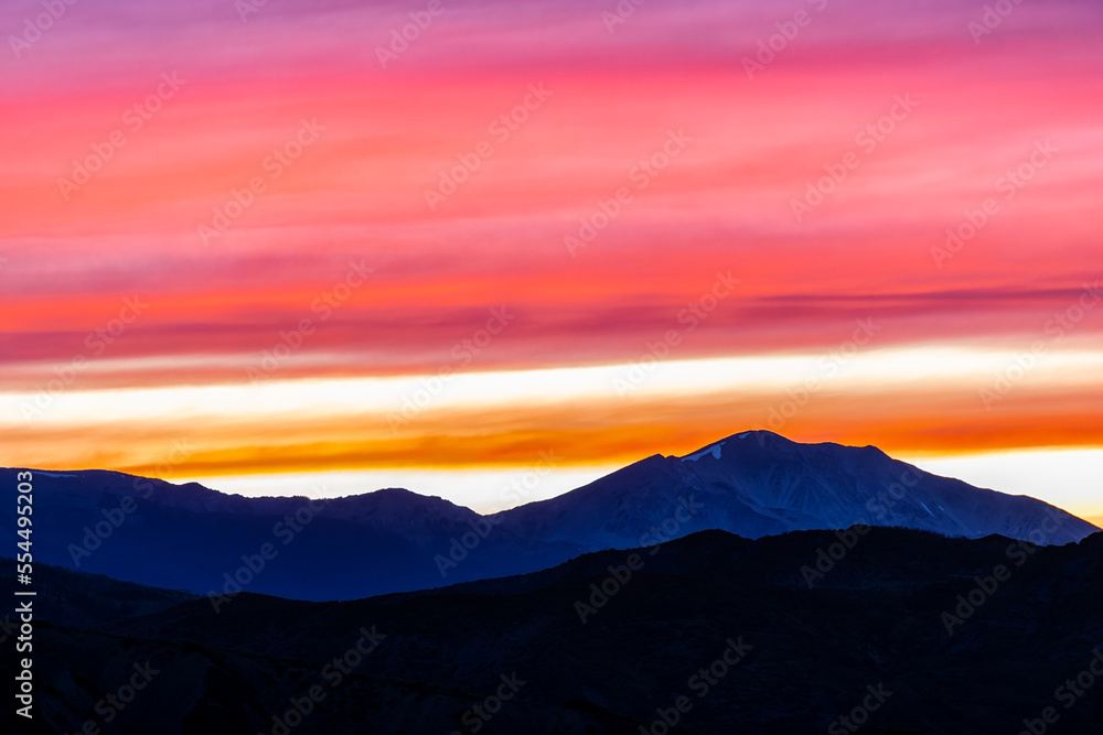 Orange red pink cloudy sunset in Aspen, Colorado with Rocky mountains peak range, vibrant color of clouds at twilight with mountain ridge silhouette