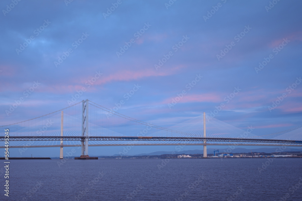 Two large bridges over the sea bay with clouds in the dawn sunlight. Forth Road Bridge and Queensferry Crossing Bridge at sunrise. Scotland, United Kingdom.