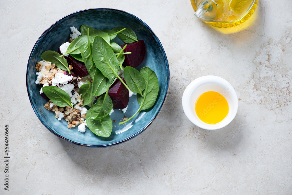 Blue bowl with fresh spinach, beetroot and goat cheese salad, flat lay on a beige stone background, horizontal shot Blue bowl with fresh spinach, beetroot and goat cheese salad, flat lay on a beige stone background, horizontal shot
