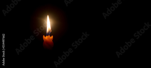 A single burning candle flame or light glowing on a beautiful spiral orange candle on black or dark background with copy space for text on table in church for Christmas  funeral or memorial service