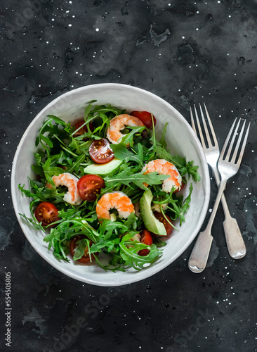 Salad with shrimp, arugula,avocado, cherry tomatoes on a dark background, top view